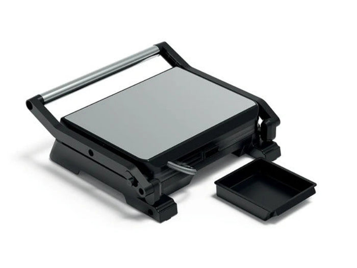 A black electric grill press with a silver heating plate, shown open with its handle raised and a small black tray beside it on a white background.