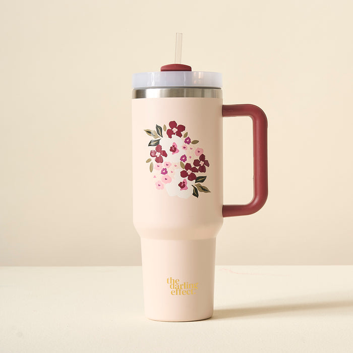 The Buds & Bloom Blush 40oz Take Me Everywhere Tumbler by The Darling Effect is a pink floral tumbler with a maroon handle, straw, and gold “the darling effect” text on the bottom.