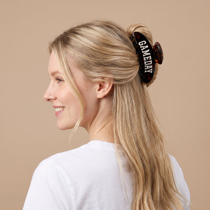 A woman with long blonde hair styled in The Darling Effect's Gameday Word Up Claw Clip smiles and looks to the side. Sporting this bold, secure accessory, she completes her look with a white t-shirt against a beige background.