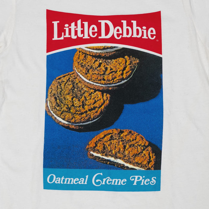Close-up of a retro design of Little Debbie Oatmeal Creme Pies. The shirt displays three oatmeal creme pies against a blue background with the "Little Debbie" logo in red at the top and "Oatmeal Creme Pies" in white text on a blue stripe at the bottom.