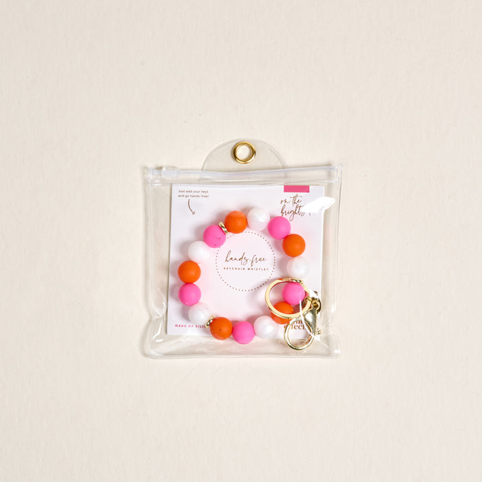The Darling Effect’s On the Brightside Hands-Free Keychain Wristlet features pink, orange, and white silicone beads with a gold clasp, packaged in a clear zip pouch with a branded card.