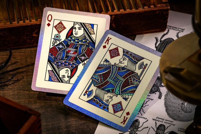 Two playing cards, Queen of Diamonds and King of Diamonds, on a wooden surface with a magnifying glass.
