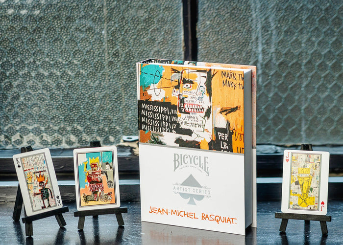 Collection of Bicycle Jean-Michel Basquiat playing cards with card stands on a reflective surface.