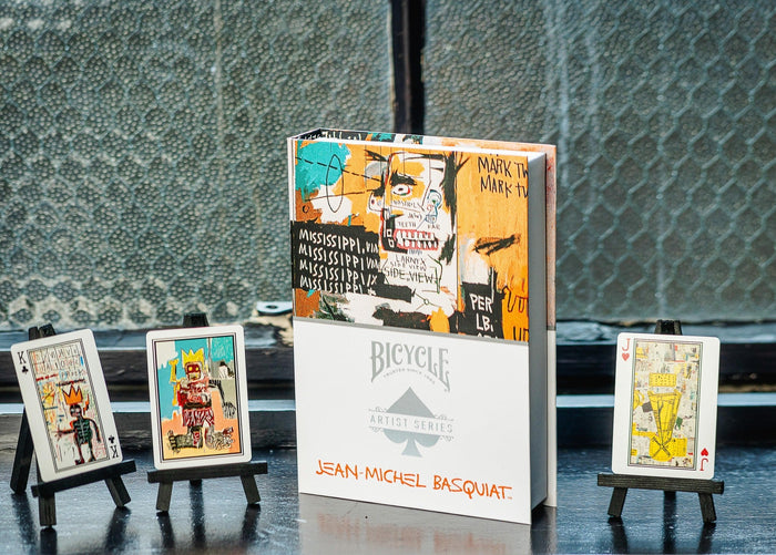Collection of Bicycle Jean-Michel Basquiat playing cards with card stands on a reflective surface.