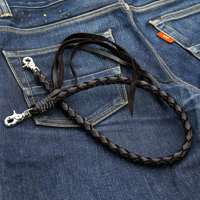The men's biker wallet chain in braided black leather laid out on a denim background.