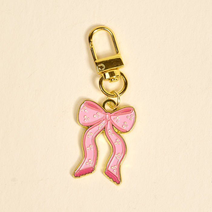 The Darling Effect Bow Pink Pawfect Collar Charm is a gold keychain featuring a pink, gold-outlined bow with white dots—perfect as an adorable pet accessory or collar charm. Pictured on a light beige background.