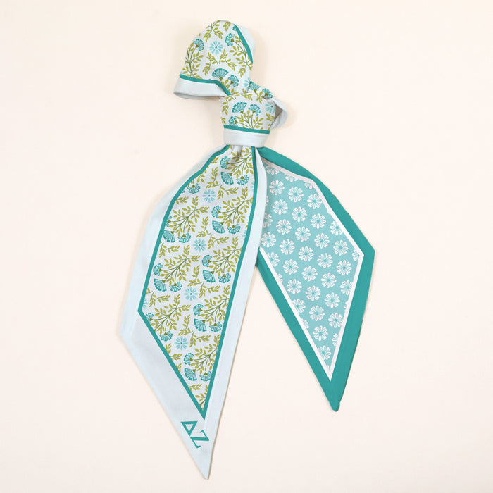 The Darling Effect's Delta Zeta Twirl & Tie Scarf Accessory features a floral and geometric pattern in light blue, teal, and green with pointed ends—an elegant piece for endless styling options.