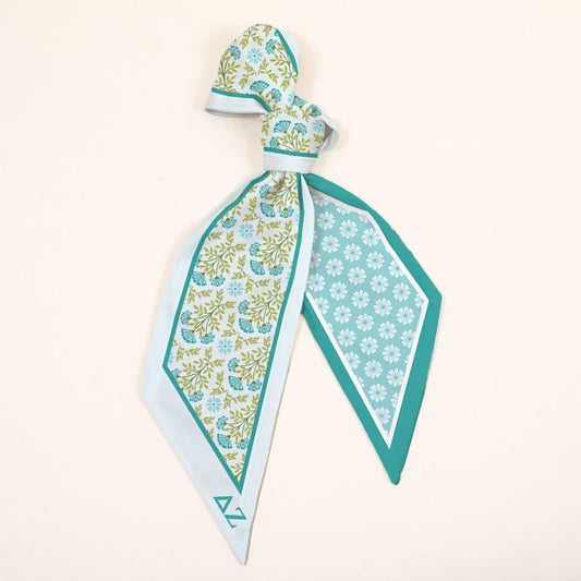 The Darling Effect's Delta Zeta Twirl & Tie Scarf Accessory features a floral and geometric pattern in light blue, teal, and green with pointed ends—an elegant piece for endless styling options.