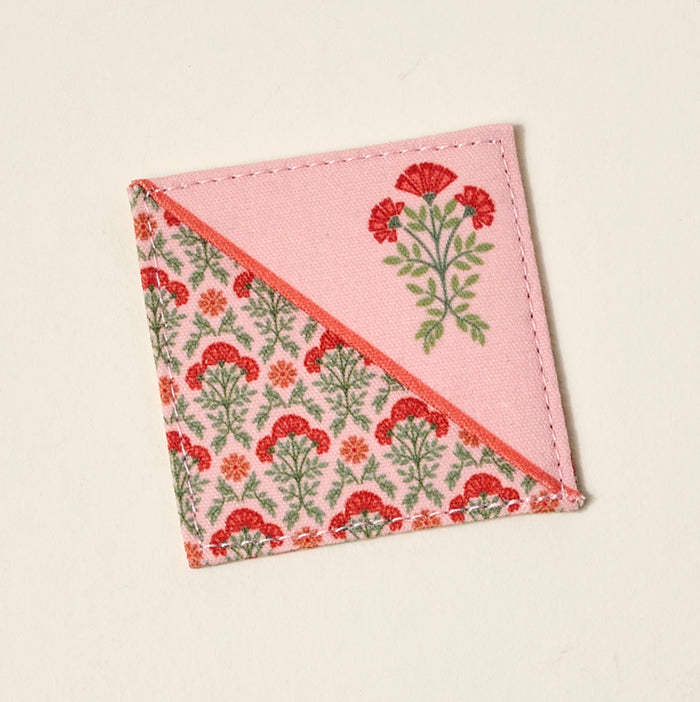 A square fabric coaster with a diagonal design—half pink with a single red carnation, half beige with red carnations—makes a pretty gift for book lovers when paired with The Darling Effect’s Everbloom Dusty Rose Corner Keeper Bookmark.