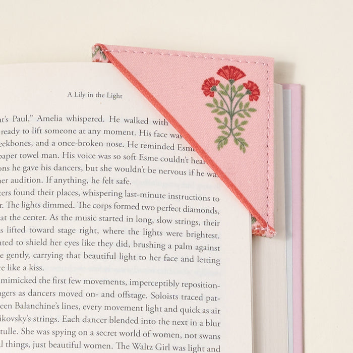 An open book with The Darling Effect’s Everbloom Dusty Rose Corner Keeper Fabric Bookmark on the top right corner, featuring quilted fabric embroidered with red flowers and green leaves, makes a charming gift for book lovers.