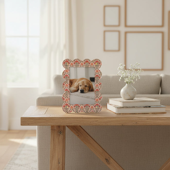 The Everbloom Dusty Rose Rectangle Scalloped Acrylic Picture Frame by The Darling Effect displays a photo of a sleeping dog on a wooden table beside stacked books and a small vase, with wall art and a sofa adding to the cozy setting.
