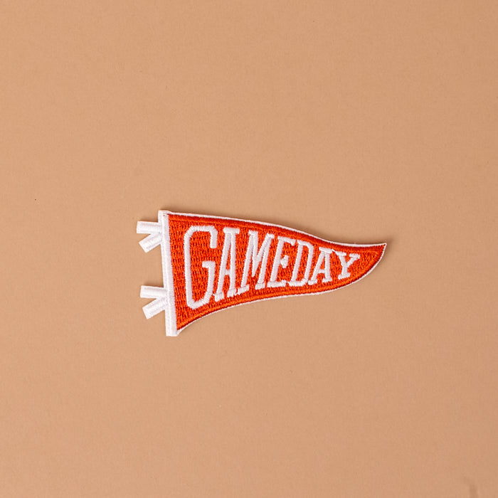 The Darling Effect’s Gameday Orange Mix & Match Iron-On Patch features an orange pennant shape with “GAMEDAY” in bold white lettering, set against a plain light brown background—an ideal choice for fans of vibrant designs who want to personalize their style with distinctive patches.