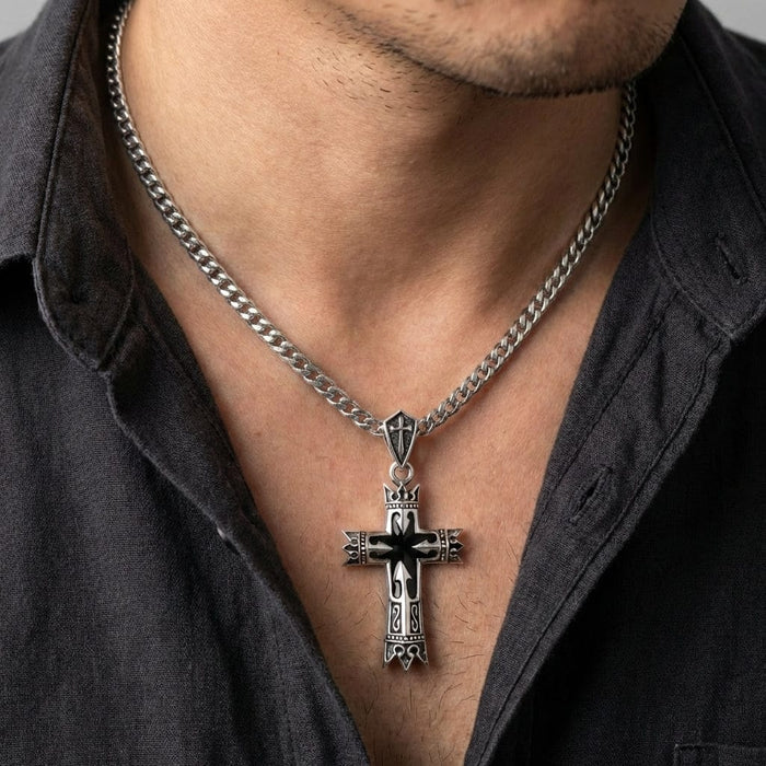 Man wearing a silver Gothic-style Guardian Knight cross pendant on a thick Cuban link chain, featuring intricate medieval-inspired engravings and black enamel details against an open gray shirt