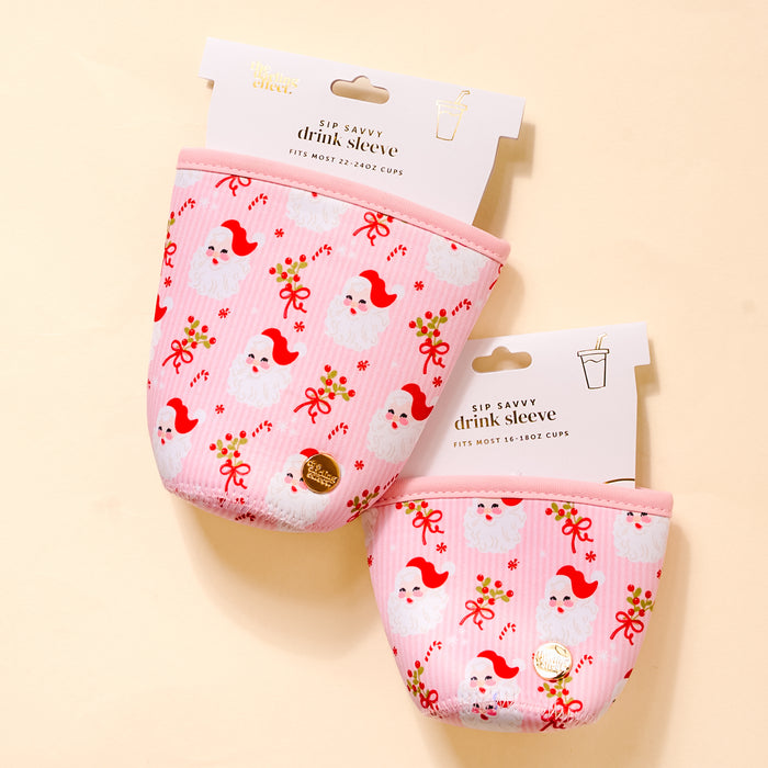 Two pink Holly Jolly Santa Sip Savvy Drink Sleeves by The Darling Effect, featuring festive Santa and holly designs, are shown on a light background. Each neoprene sleeve has a white label and fits 16-18 oz and 22-24 oz cups.