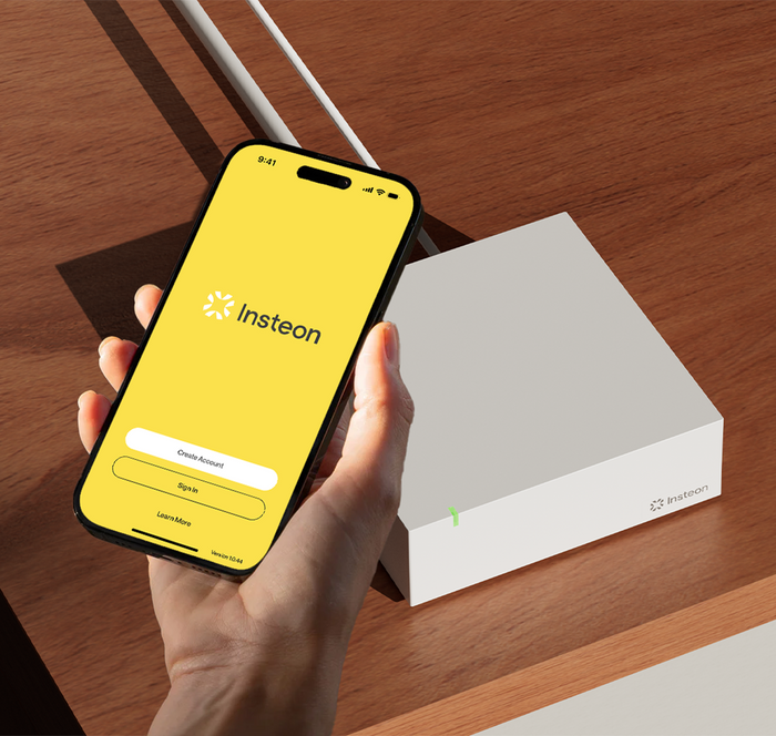 A hand holding a phone over the Insteon Hub device