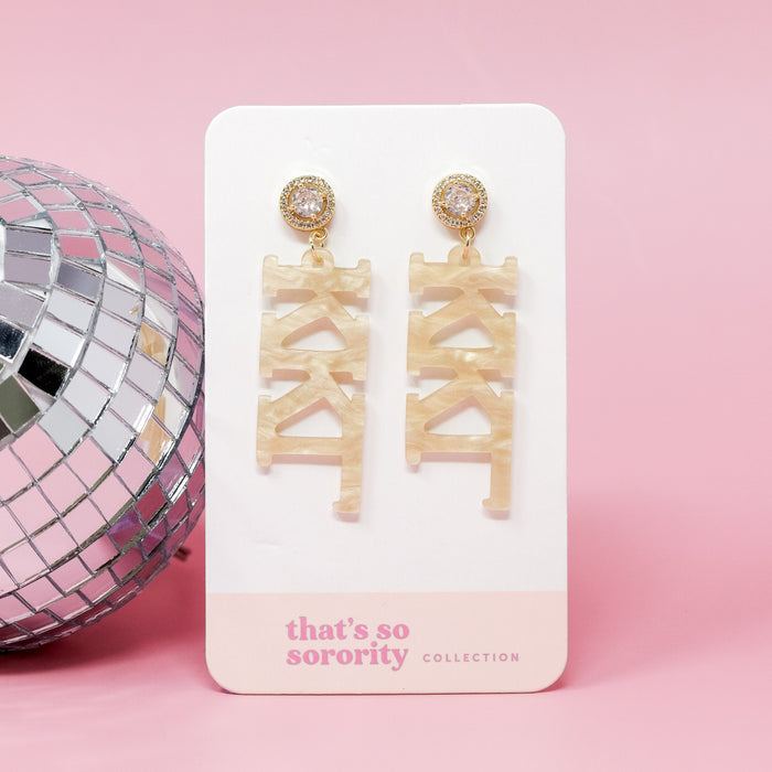 Kappa Kappa Gamma Letter Gold Acrylic Earrings by The Darling Effect feature gold and pearl studs with beige marbled Greek letter charms—ideal for bid-day or sisterhood events. Displayed on a "that's so sorority collection" card with a pink disco ball backdrop.