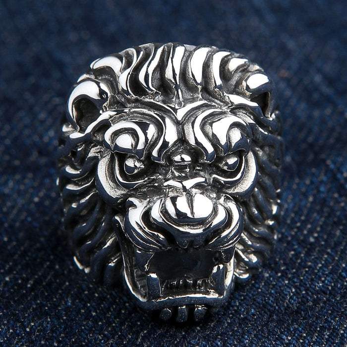 A solid sterling silver lion head biker ring with a powerful roaring expression, shown on a denim background.