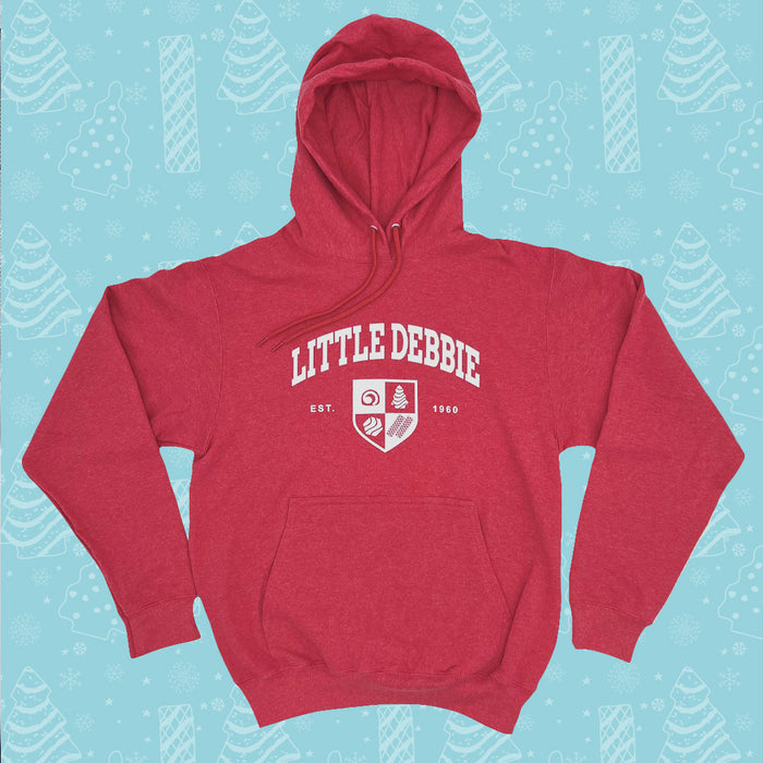 Little Debbie University Red hoodie with the words 'LITTLE DEBBIE' printed in white on the front, accompanied by a shield emblem containing various symbols and the text 'EST. 1960'. The hoodie has a front pocket and a hood with drawstrings. It's set against a light blue background patterned with white illustrations of Christmas Trees Cakes, Christmas Tree Brownies, snowflakes, and other winter motifs.