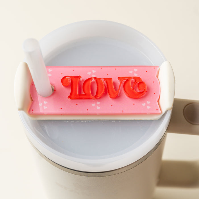 The Darling Effect’s Love Tumbler Lid Tag is a pink, rectangular accessory with red “LOVE” lettering and small hearts—perfect for personalizing your Stanley Quencher 2.0 tumbler lid.
