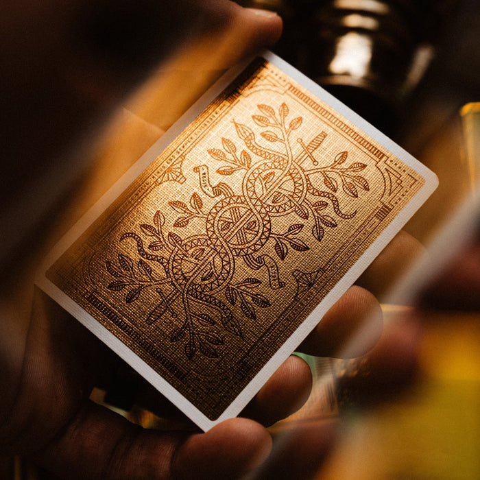 Close-up of a hand holding a deck of gold foiled playing cards with intricate design.
