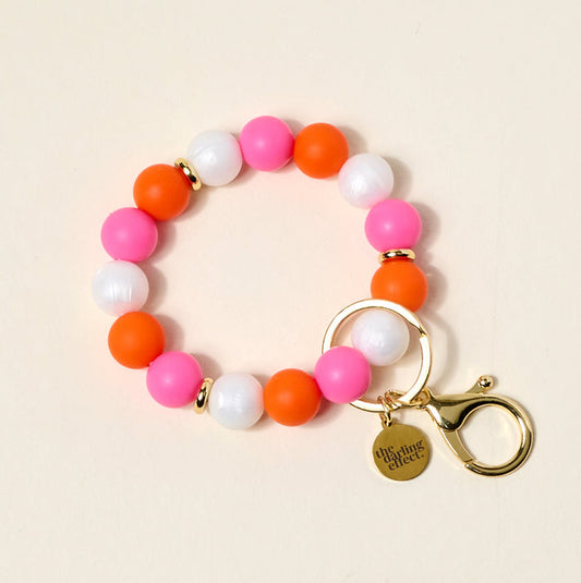 The Darling Effect's On the Brightside Hands-Free Keychain Wristlet features pink, orange, and white silicone beads, a gold clasp, keyring, and a "the darling effect" charm—keeping your keys stylish and hands-free.