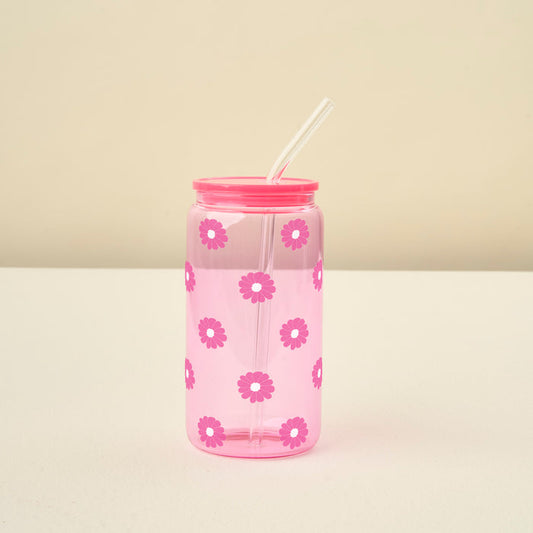 The Darling Effect Pink Color Glass Round Cup with pink daisy details, a matching pink lid, and a glass straw rests on a white surface against a beige background.
