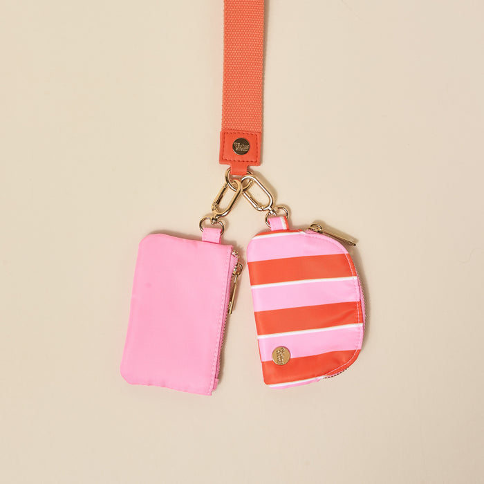 The Darling Effect Sicily Stripes Pink Dynamic Duo Pouch Wristlet features pink and orange striped zippered pouches hanging hands-free from an orange strap with gold clips.