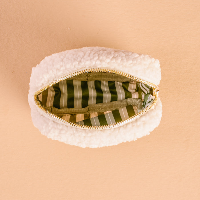 The Square Twinkling Tree Teddy Pouch by The Darling Effect, a small white sherpa pouch, is open to reveal its green interior lining with white and tan vertical stripes, set against a peach-colored background.