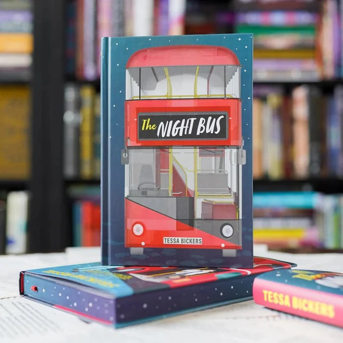The Night Bus LitJoy Crate Edition hardcover book by Tessa Bickers standing upright, featuring a custom cover with a red double-decker London bus illustration on a dark navy starry night background. Two copies lie flat beneath it in front of a blurred colorful bookshelf.