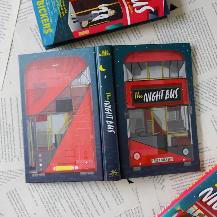 Flat lay of The Night Bus LitJoy Crate Special Edition hardcover by Tessa Bickers lying open on newspaper pages, showing the front cover with red double-decker bus illustration, the dark navy spine with crescent moon and LitJoy logo, and the back cover with bus interior cross-section design. The standard paperback editions are visible in the corners.