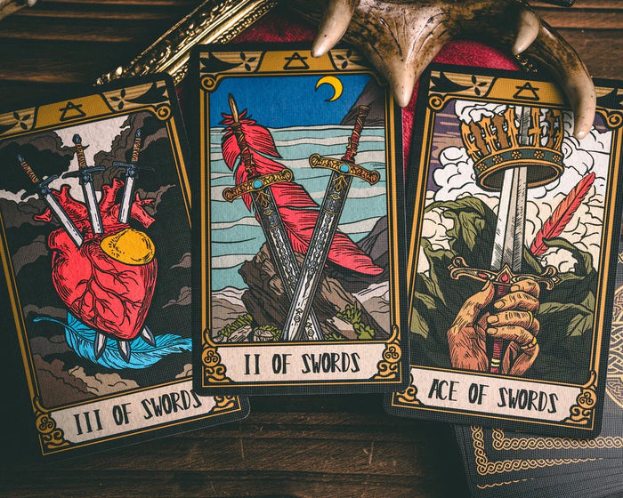 Three tarot cards titled 'III of Swords', 'II of Swords', and 'Ace of Swords' on a wooden surface.