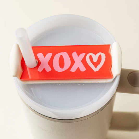 A close-up of The Darling Effect's XOXO Tumbler Lid Tag—a red silicone cover with pink and white XOXO and heart design—perfect as a cute personalized accessory for your Stanley Quencher 2.0 lid.